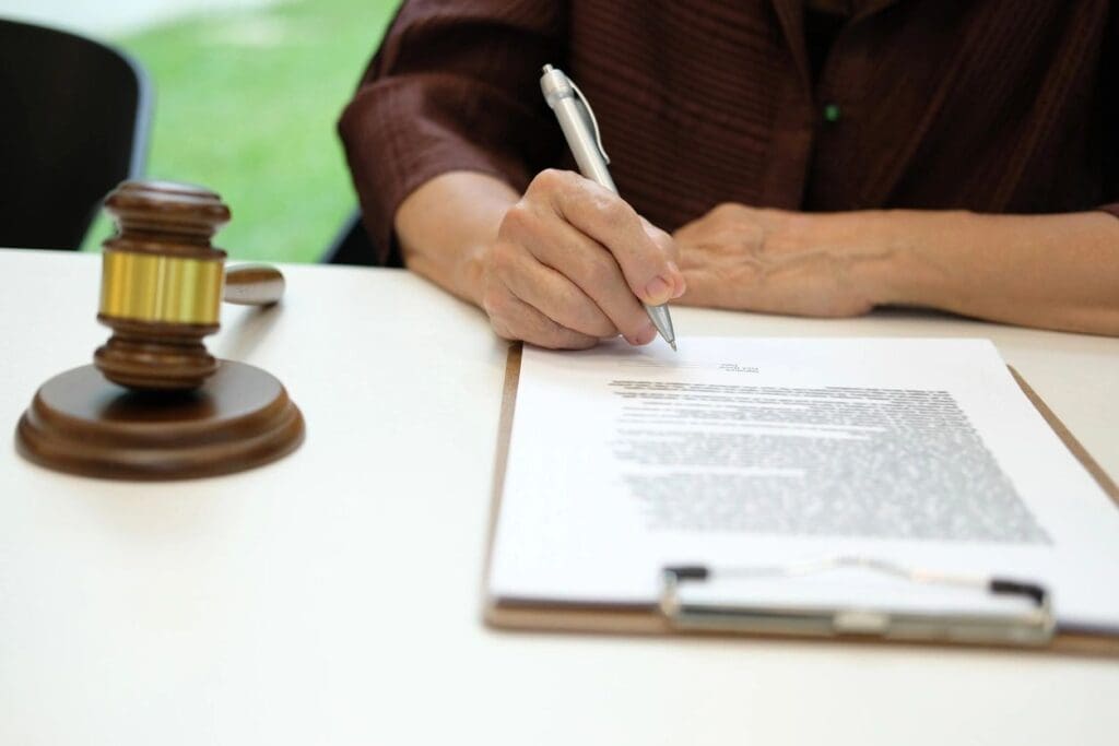 A person signing a legal document with a gavel nearby.
